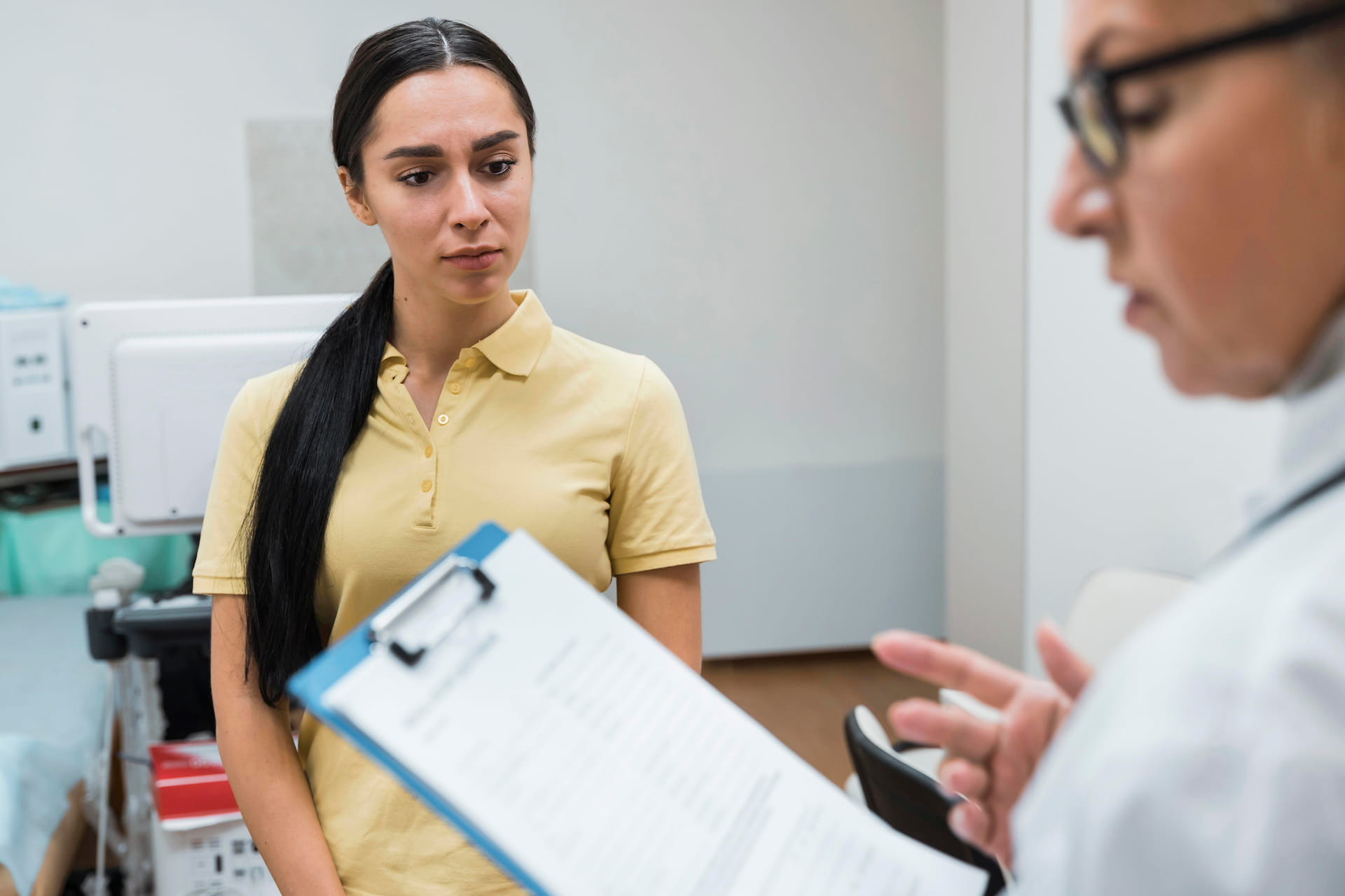 A concerned young woman listens closely to a doctor holding a clipboard, reflecting the patient-doctor care at Immedex.