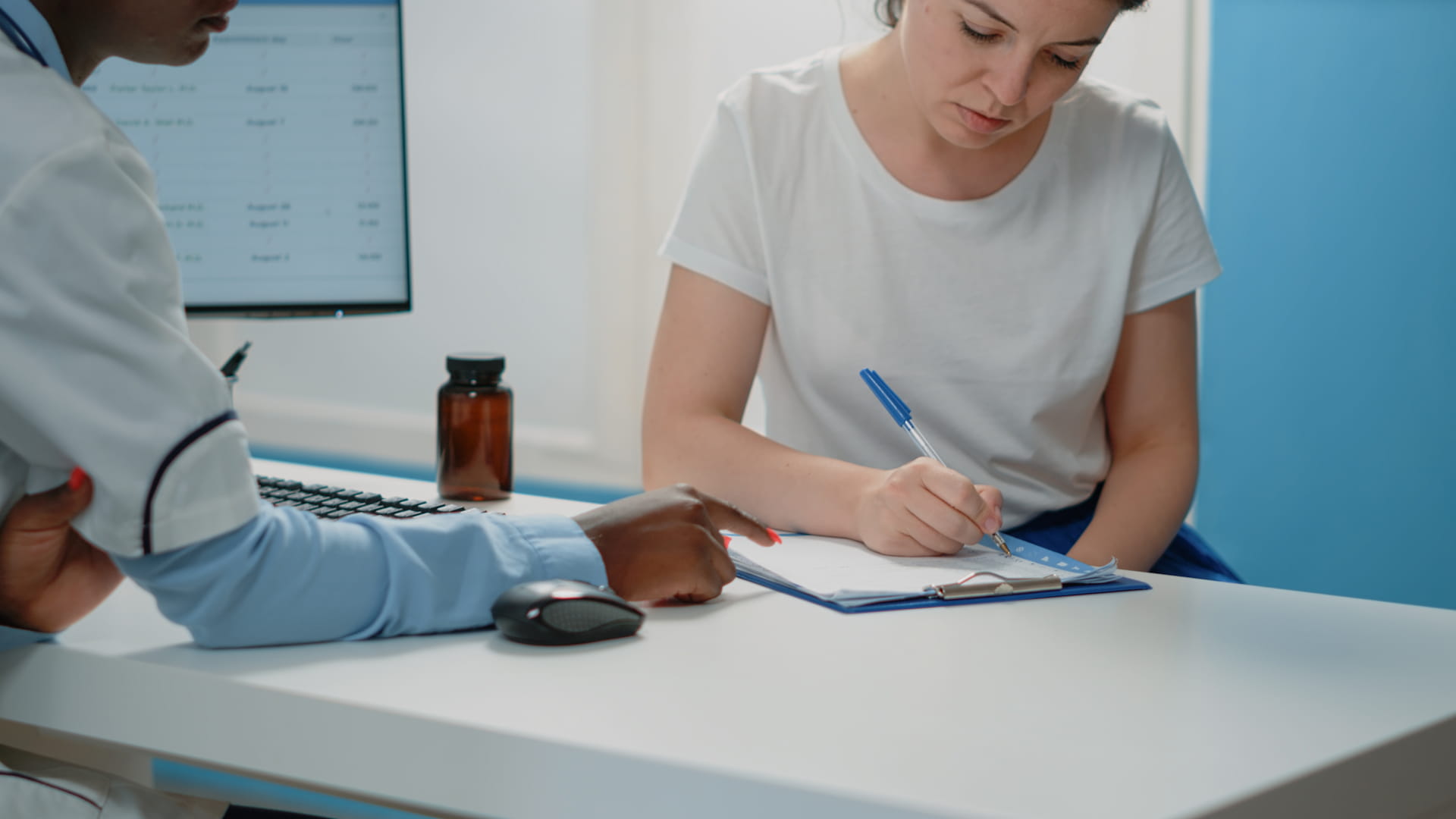 An adult woman signs a clipboard as a medical professional points to a section, illustrating Immedex’s streamlined patient care process.