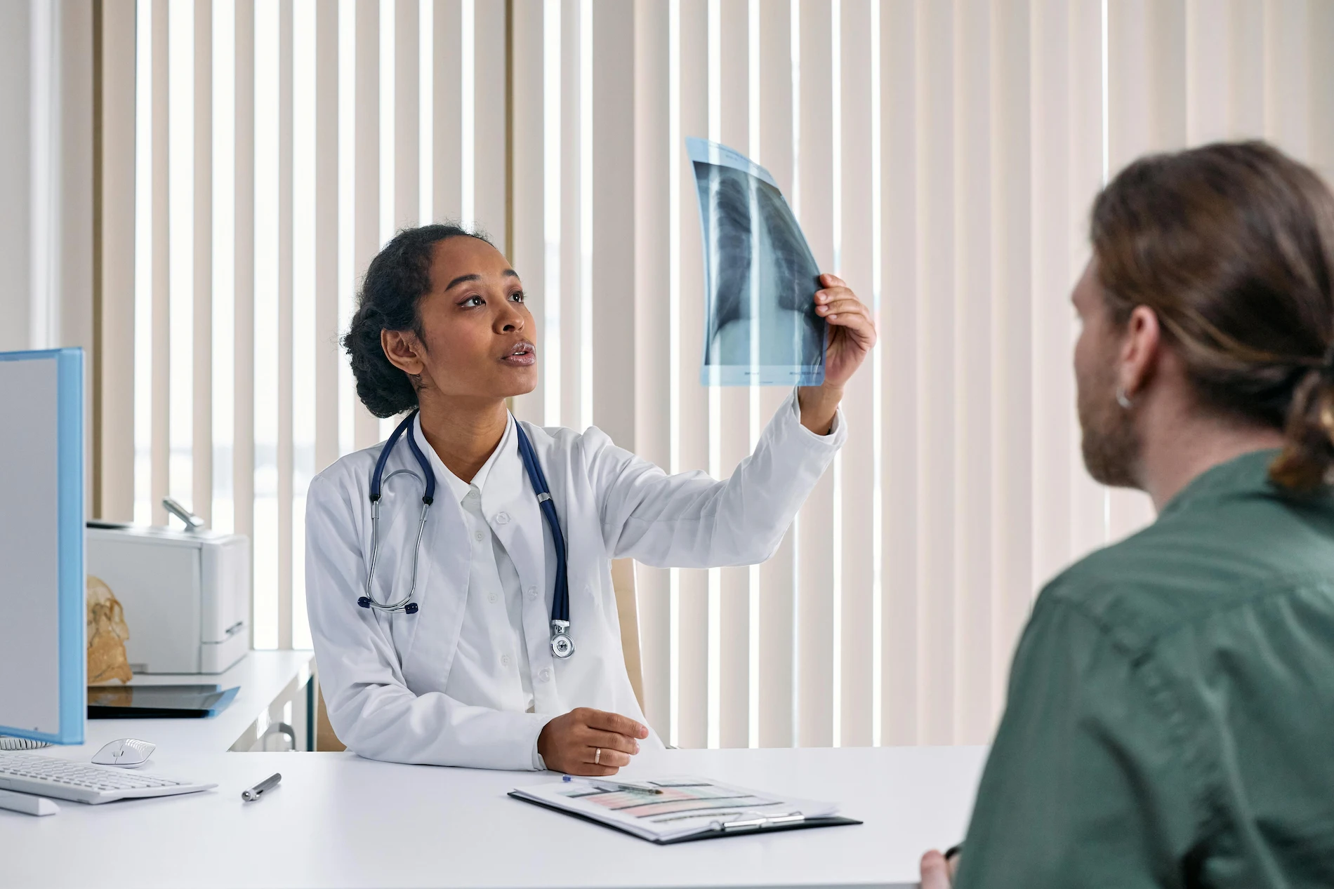 A female doctor holding up a chest X-ray from his IME to a patient sitting across from her.